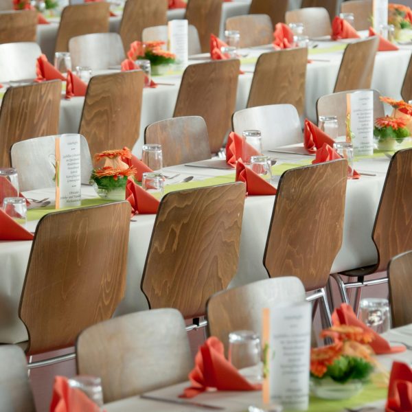 Beautifully arranged tables with wooden chairs for a formal event, adorned with orange flowers.